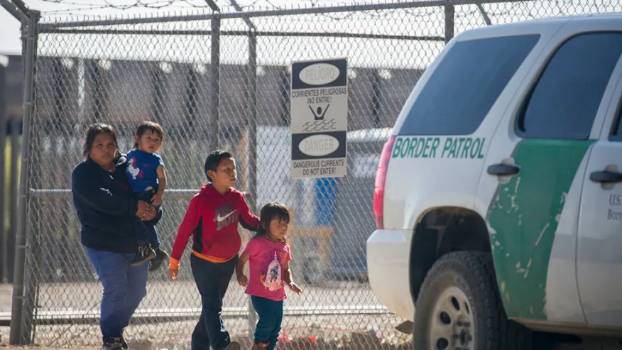 a mother with her children walking past a U.S. Border Patrol vehicle at the U.S. southern border